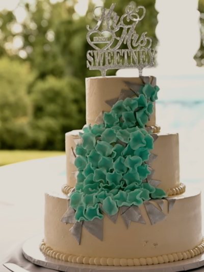 A tiered wedding cake trimmed with green sugar ruffles, set beside a pool