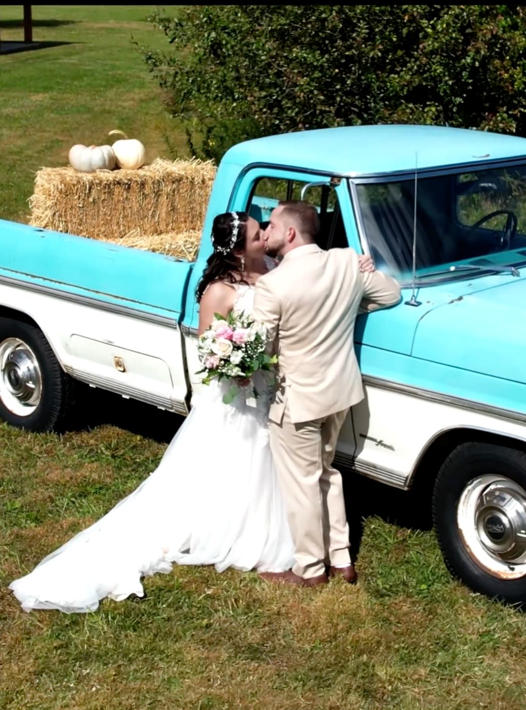 A bride and groom kissing beside a vintage turquoise pickup truck in an open field