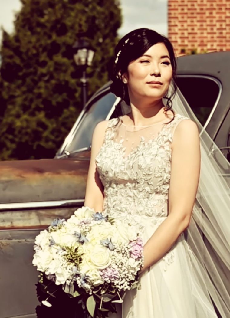 A bride holding her bouquet beside a vintage car, her veil trailing behind her