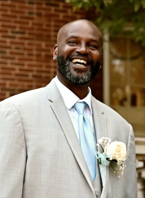 A groom laughing in a pale suit outside a brick venue