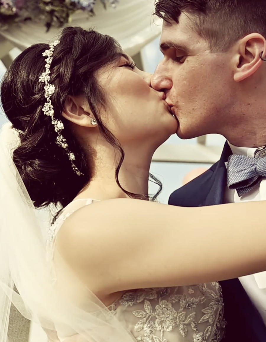 A bride and groom kissing beneath a white ceremony arch dressed with flowers